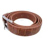 کمربند چرمی رنگ عسلی طرح کروکدیلی با سگک نقره ای که به صورت حلقوی روی پس زمینه سفید هستش