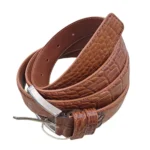 کمربند چرمی رنگ عسلی طرح کروکدیلی با سگک نقره ای که به صورت گرد شده کمی با زاویه بیرون زدگی روی پس زمینه سفید هستش