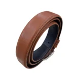 کمربند چرمی رنگ عسلی طرح صاف با سگک نقره ای که به صورت حلقوی ایستاده روی پس زمینه سفید هستش